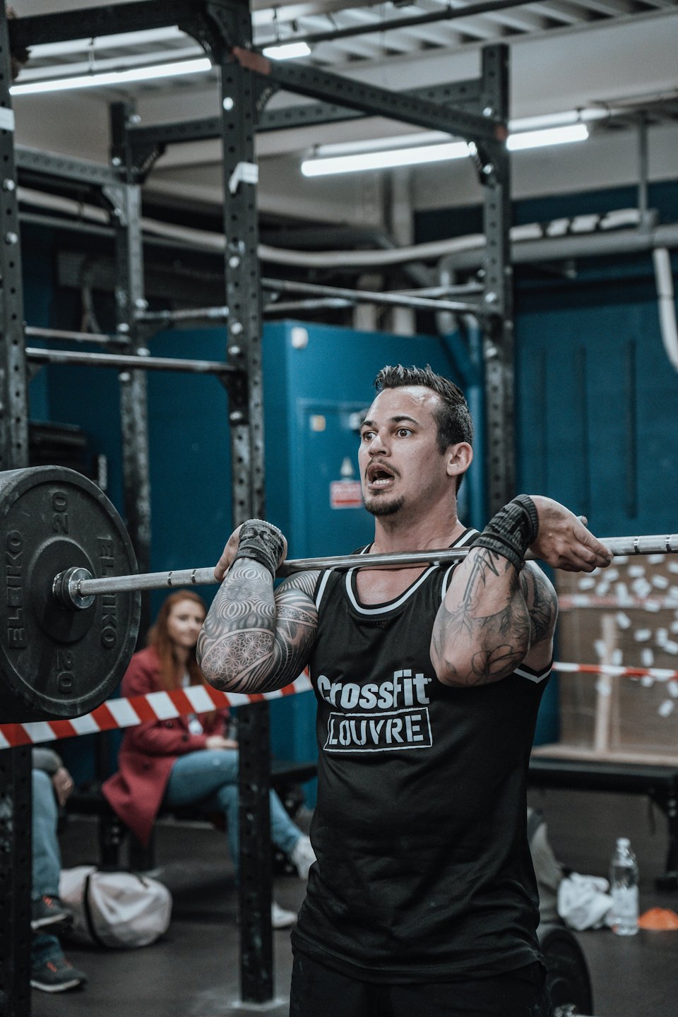 Tattooed man performing a barbell lift in a gym.