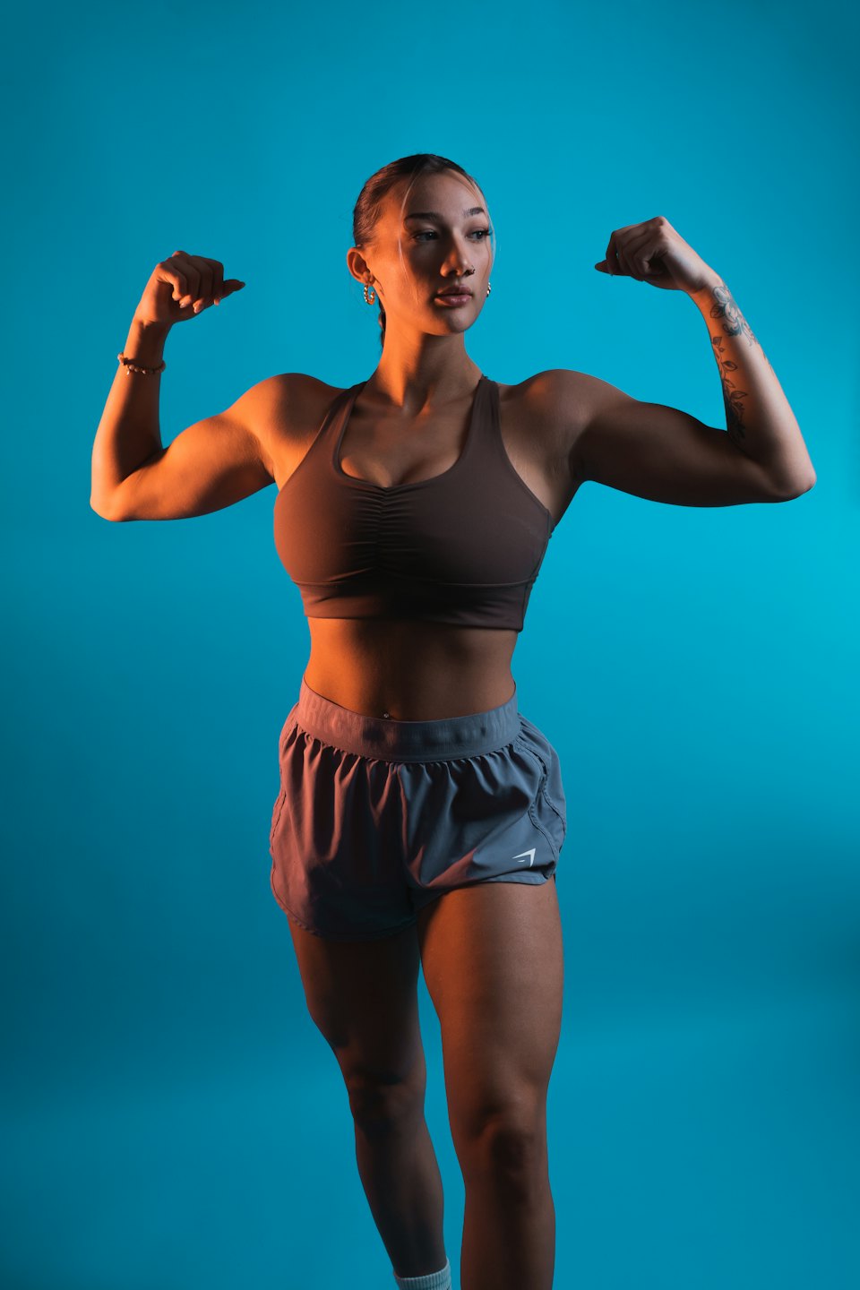 Athletic woman in sports bra flexing biceps in studio.